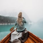 woman in gray hoodie sitting on brown wooden boat on lake during daytime